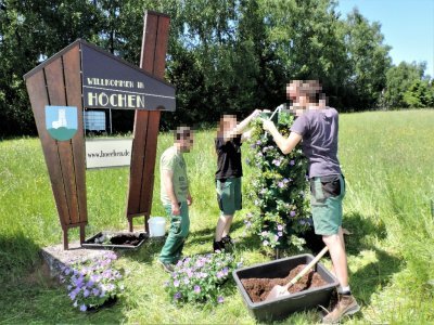 Drei Auszubildende des Christlichen Jugenddorfes (CJD) Homburg stellten Mitte Mai mit dem Gärtnermeister Christian Pfeil eine Blumensäule mit Petunien am Dorfeingang aus Richtung Jägersburg/Waldmohr auf.